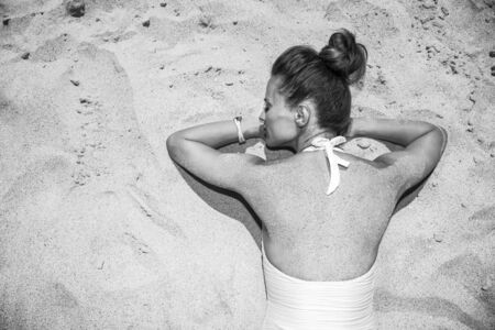 Warm sand treatment. Seen from behind woman in swimsuit laying on the sandの写真素材