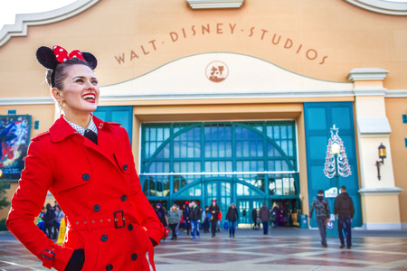 DISNEYLAND, FRANCE - DECEMBER, 8, 2016:. happy elegant woman in red trench coat in the front of Disney Studio 1 looking into the distanceのeditorial素材