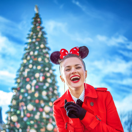 DISNEYLAND, FRANCE - DECEMBER, 8, 2016: smiling stylish woman in red trench coat in the front of big Christmas treeのeditorial素材