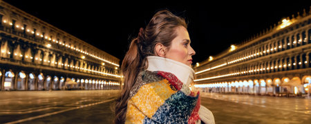 Classical tourist enjoyment in Venice, Italy.  Portrait of elegant tourist woman wrapped in a long scarf at San Marco square in Venice, Italy in the winter looking asideの写真素材