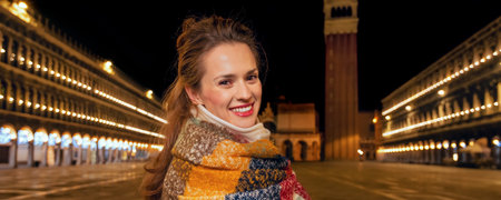 Classical tourist enjoyment in Venice, Italy.  Portrait of happy elegant traveller woman wrapped in a long scarf at San Marco square in Venice, Italy in the winter standing near St Mark's Campanileの写真素材