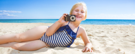 Sun kissed beauty. smiling healthy child in beachwear on the seacoast with digital camera taking photoの写真素材