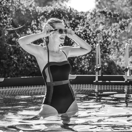 Fun weekend alfresco. smiling healthy woman in blue swimsuit in the swimming pool in sunglassesの写真素材