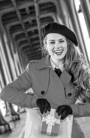 happy young tourist woman in red trench coat on Pont de Bir-Hakeim bridge in Paris showing shopping bag and Christmas present boxの写真素材