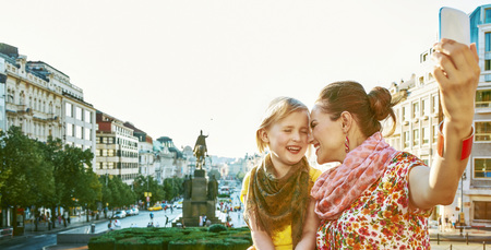 The spirit of old Europe in Prague. smiling young mother and child tourists on Vaclavske namesti in Prague, Czech Republic with phone taking selfieの写真素材