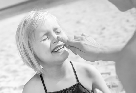 Sun kissed beauty. happy young mother and daughter in swimsuit on the beach applying SPFの写真素材