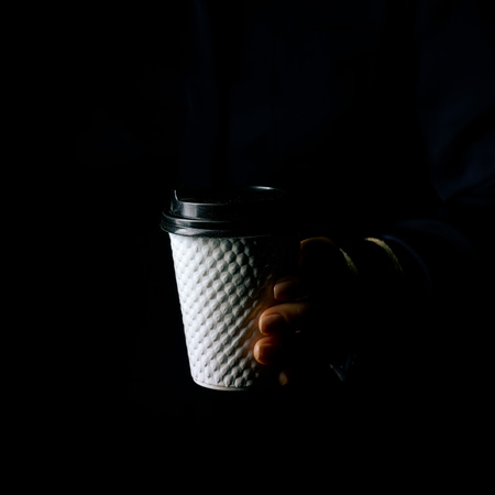 Black Mania. woman hand isolated on black showing paper coffee cupの写真素材