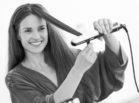 Happy young woman straightening hair with straightenerの写真素材