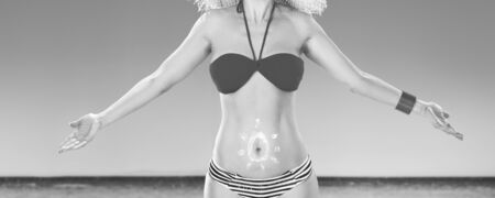 Perfect summer. smiling active woman on the seashore with sun drawn by spf creme on the stomachの写真素材