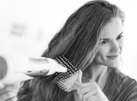 Happy woman brushing and blow drying hair in bathroomの写真素材