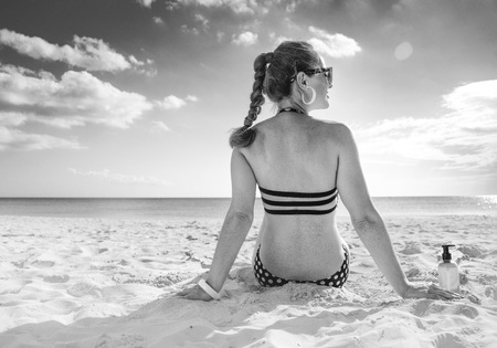 Sun kissed beauty. Seen from behind healthy woman in beachwear on the seashore looking into the distanceの写真素材