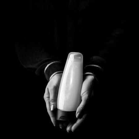 Black Mania. female hands isolated on black showing a bottle of cosmeticsの写真素材