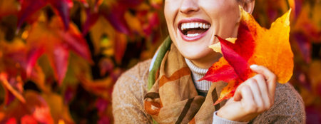Closeup on smiling young woman with autumn leafs in front of foliageの写真素材