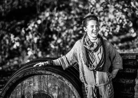 Portrait of smiling young woman near wooden barrel in autumn outdoorsの写真素材