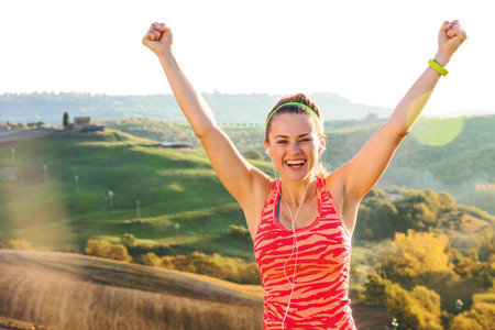 Fitness and magical views of Tuscany. Portrait of smiling active active woman in sports gear against scenery of Tuscany rejoicingの写真素材