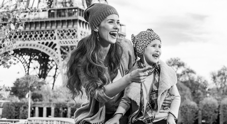 Autumn getaways in Paris with family. happy mother and daughter tourists on embankment in Paris, France pointing on something while sitting on the parapetの写真素材