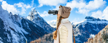 Winter on higher level of fun. Seen from behind stylish traveller woman against mountain scenery in...