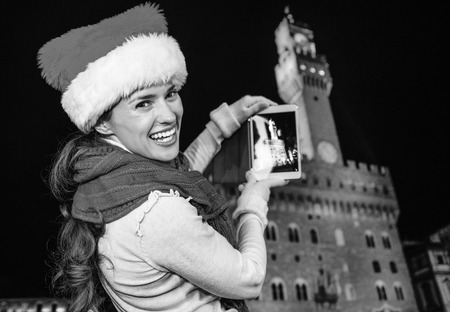 Trip full of inspiration at Christmas time in Florence. smiling young woman in Christmas hat in Florence, Italy taking photo with tablet PCの写真素材