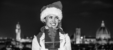 Trip full of inspiration at Christmas time in Florence. happy young woman in Christmas hat in Florence, Italy with Christmas present box looking asideの写真素材
