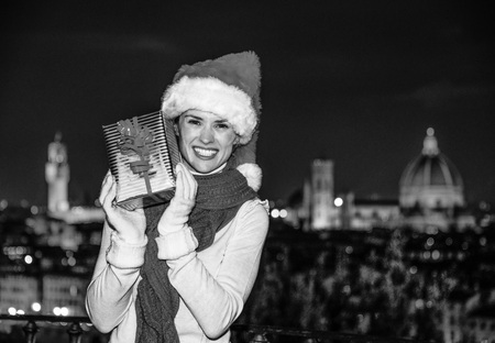 Trip full of inspiration at Christmas time in Florence. happy young woman in Christmas hat at Piazzale Michelangelo in Florence, Italy showing Christmas present boxの写真素材
