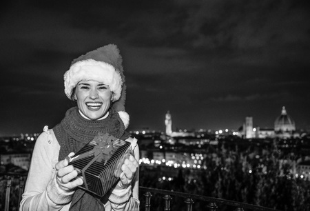 Trip full of inspiration at Christmas time in Florence. Portrait of happy young woman in Christmas hat in Florence, Italy with Christmas present boxの写真素材