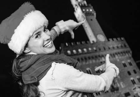 Trip full of inspiration at Christmas time in Florence. smiling modern woman in Christmas hat against Palazzo Vecchio in Florence, Italy framing with handsの写真素材