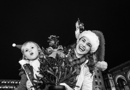 Trip full of inspiration at Christmas time in Florence. Portrait of relaxed young mother and child travellers in Christmas hats in Florence, Italy with Christmas tree having fun timeの写真素材