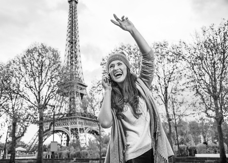 Autumn getaways in Paris. happy young woman in Paris, France using a mobile phone and handwavingの写真素材