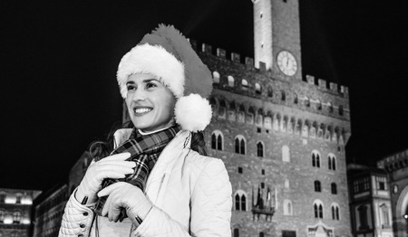 Trip full of inspiration at Christmas time in Florence. smiling young woman in Christmas hat in the front of Palazzo Vecchio in Florence, Italy looking into the distanceの写真素材
