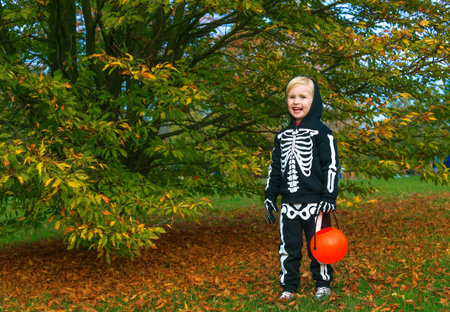 Trick or Treat. Full length portrait of happy child wearing skeleton costume on Halloween at the park with pumpkin Jack OLantern basketの写真素材