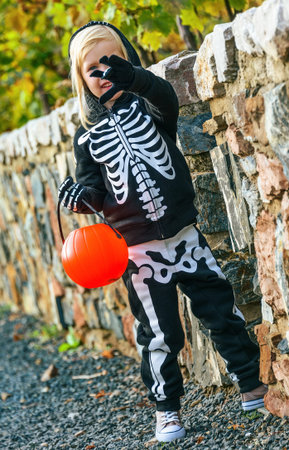 Trick or Treat. child wearing skeleton costume on Halloween outdoors pumpkin Jack O’Lantern basket...