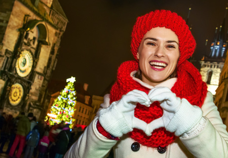Magic on streets of the old town at Christmas. smiling young tourist woman in red hat and scarf at Christmas on Old Town Square in Prague Czech Republic showing heart shaped handsの写真素材