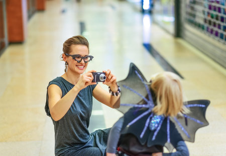 Trick or Treat. happy modern mother and daughter in bat costumes on Halloween at the mall with digital camera taking photoの写真素材