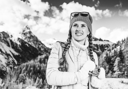 Winter on higher level of fun. happy modern traveller woman in South Tyrol, Italy with vintage photo camera looking into the distanceの写真素材