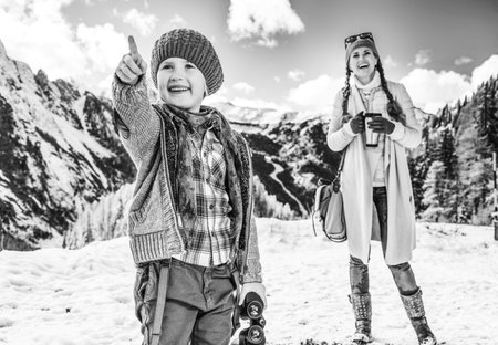 Winter on higher level of fun. modern mother and child tourists in the front of mountain scenery in...