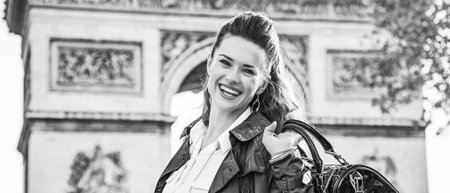 Stylish autumn in Paris. Portrait of smiling young elegant woman in trench coat near Arc de Triomphe in Paris, Franceの写真素材