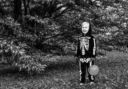 Trick or Treat. Full length portrait of happy child wearing skeleton costume on Halloween at the park with pumpkin Jack OâLantern basketの写真素材
