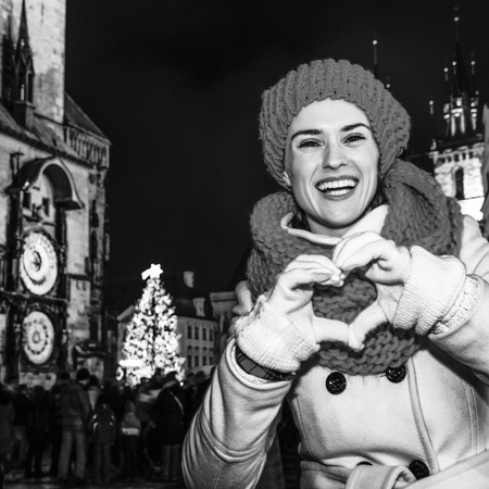 Magic on streets of the old town at Christmas. smiling young tourist woman in red hat and scarf at Christmas on Old Town Square in Prague Czech Republic showing heart shaped handsの写真素材