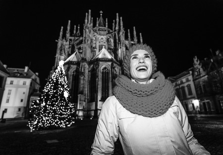 Magic on streets of the old town at Christmas. happy young woman in red hat and scarf near Christmas tree in the front of St. Vitus Cathedral in Prague Czech Republic looking upの写真素材