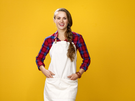 Healthy food to your table. Portrait of happy young woman farmer wearing apron isolated on yellowの写真素材