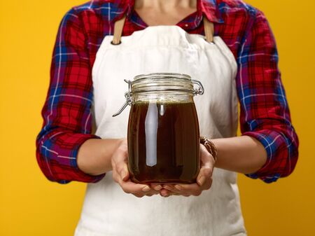 Healthy food to your table. Closeup on modern woman cook wearing apron isolated on yellow showing jar with honeyの写真素材