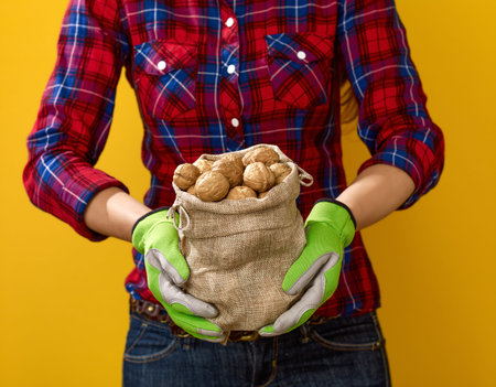 Healthy food to your table. Closeup on modern woman farmer in checkered shirt on yellow background showing walnutの写真素材