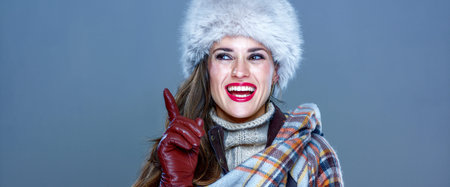 Winter things. Portrait of smiling elegant woman in fur hat isolated on cold blue got idea