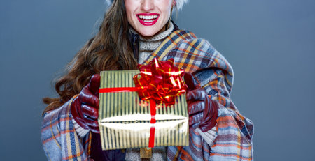 Winter things. Closeup on smiling trendy woman in fur hat isolated on cold blue background giving present boxの写真素材