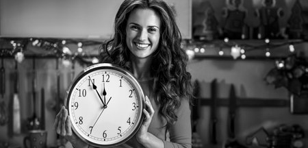 Happy young housewife showing clock in christmas decorated kitchen