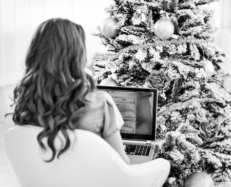Woman using laptop near christmas tree . rear viewの写真素材