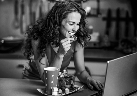 Happy young housewife with christmas snacks using laptop in kitchenの写真素材