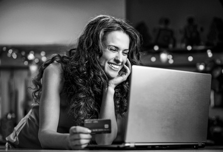 Happy young woman holding credit card and choosing gifts on laptopの写真素材