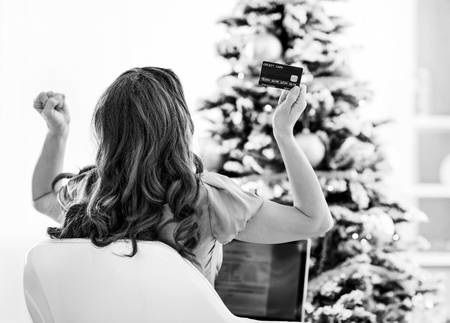 Young woman with credit card and laptop rejoicing success near christmas treeの写真素材
