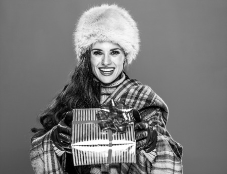 Winter things. Portrait of smiling trendy woman in fur hat isolated on cold blue background giving present boxの写真素材